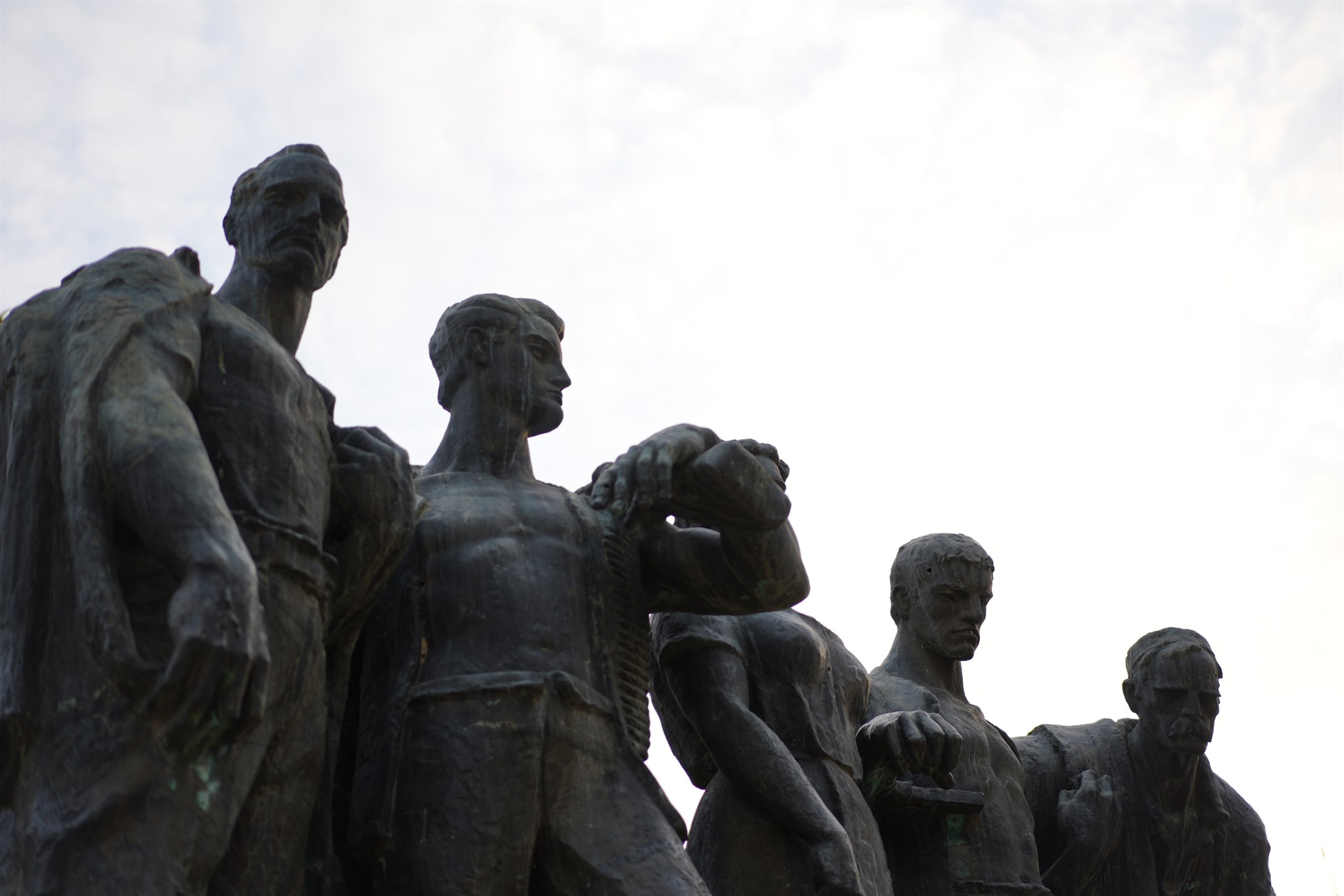A bronze partisan monument group seen from below against a pale, clouded sky.