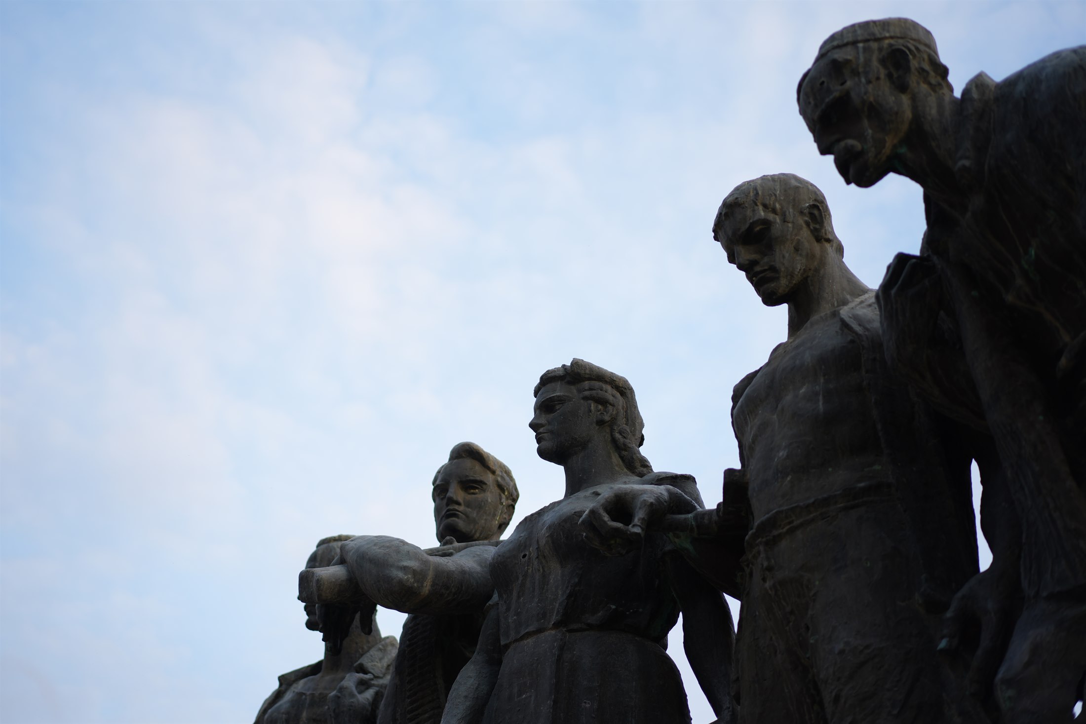 A bronze partisan monument group seen from below against a clear blue sky.