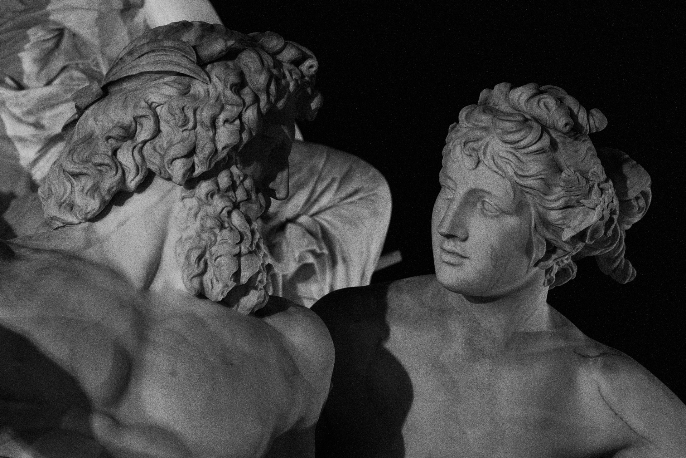 Two marble heads at night — a bearded elder in shadow beside a younger figure catching the light.